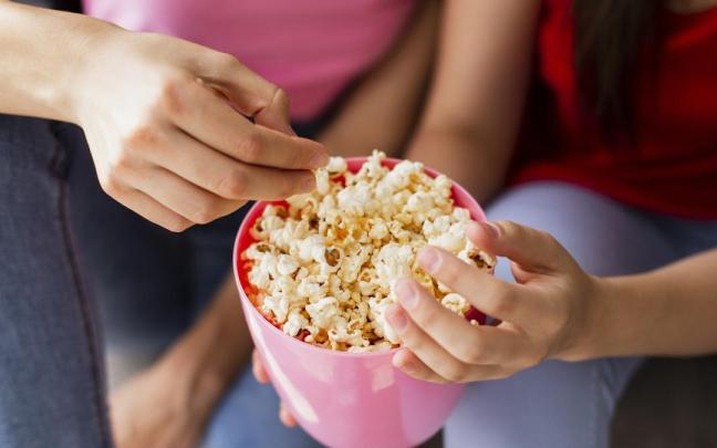 Dos personas comparten un bol de palomitas caseras. Dos personas comparten un bol de palomitas caseras.