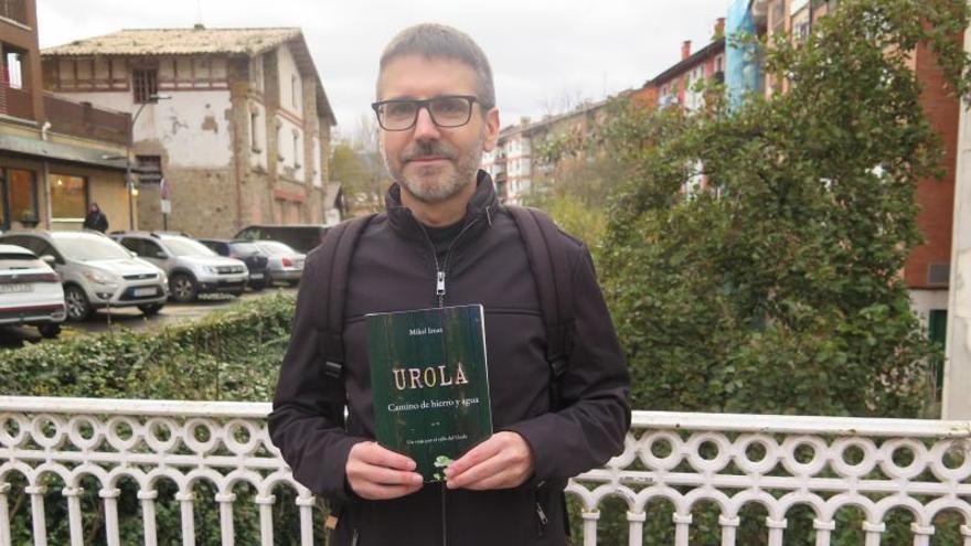 Mikel Imaz, con su libro, en el puente del Isabel: a la izquierda la estación del Urola y a la derecha la casa donde vivía cuando inició el proyecto.