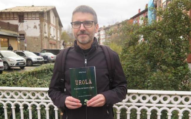 Mikel Imaz, con su libro, en el puente del Isabel: a la izquierda la estación del Urola y a la derecha la casa donde vivía cuando inició el proyecto.