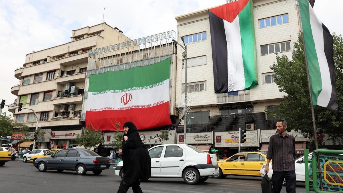 Iraníes caminan frente a varias banderas de Palestina e Irán colgadas de un edificio en Teherán.