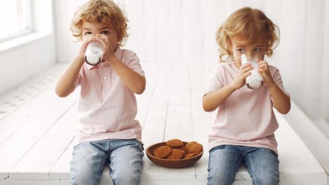 Niños toman un vaso de leche con galletas.