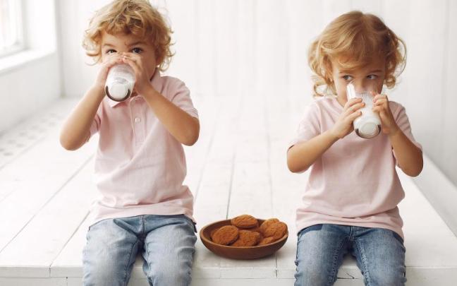 Niños toman un vaso de leche con galletas.