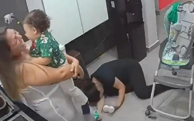 La madre muerta de risa en el suelo y su amiga con el bebé.