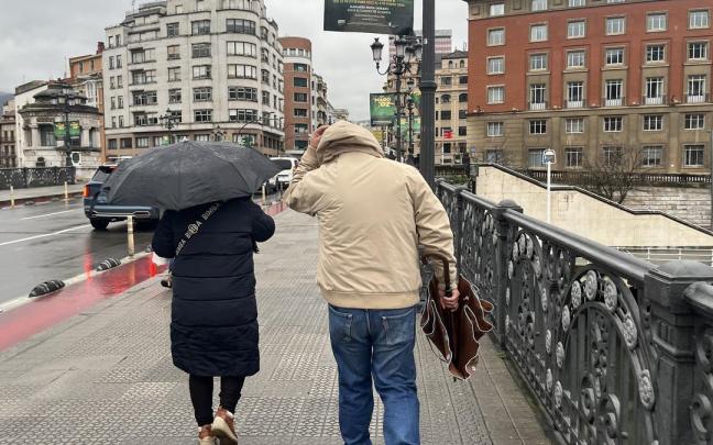 Dos personas se protegen del viento en Bilbao.