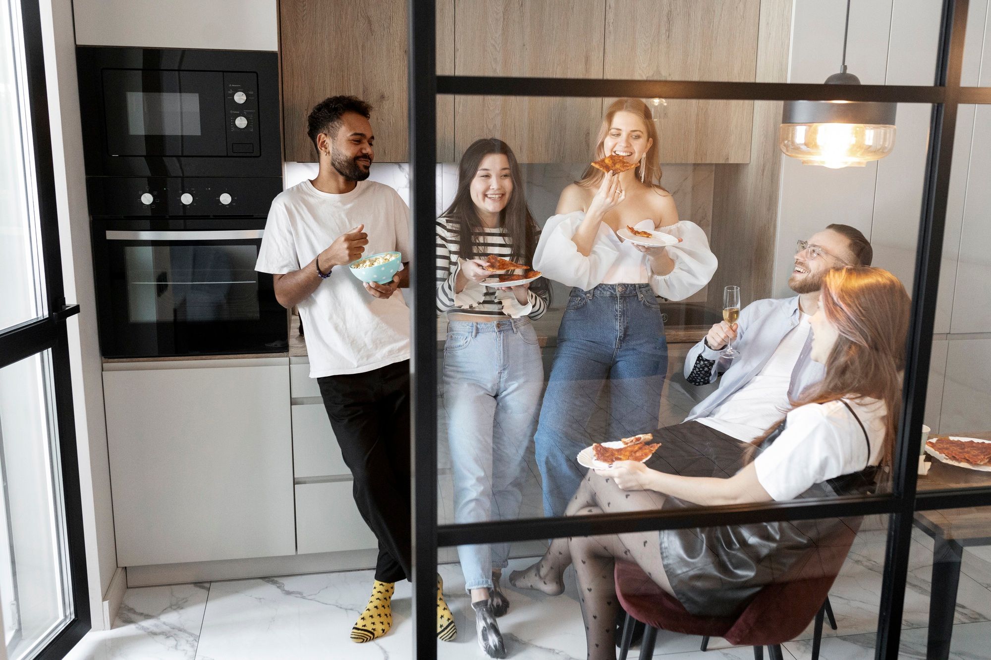 Un grupo de amigos come pizza en la cocina de un apartamento.