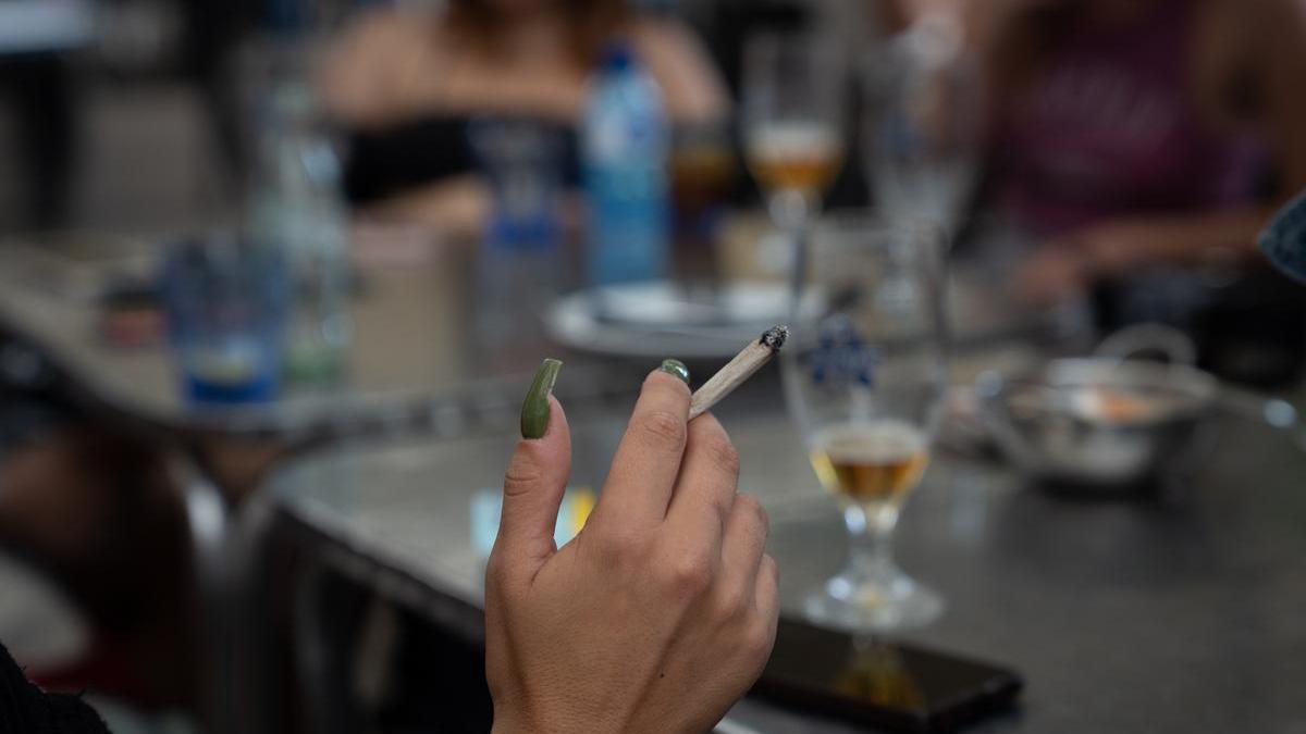 Una mujer fuma un cigarro sentada en una terraza.