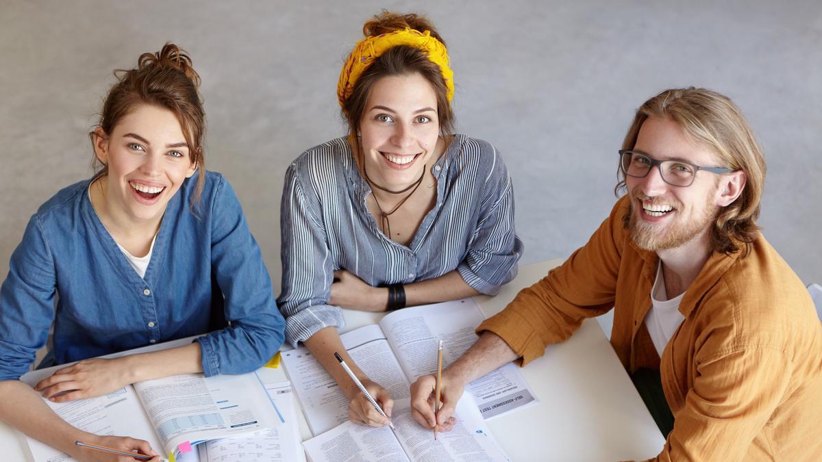 Tres compañeros comparten mesa en una oficina.