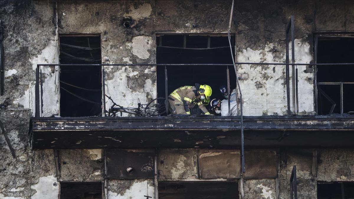 Los bomberos inspeccionan un cuerpo en un balcón del edificio incendiado en Valencia.