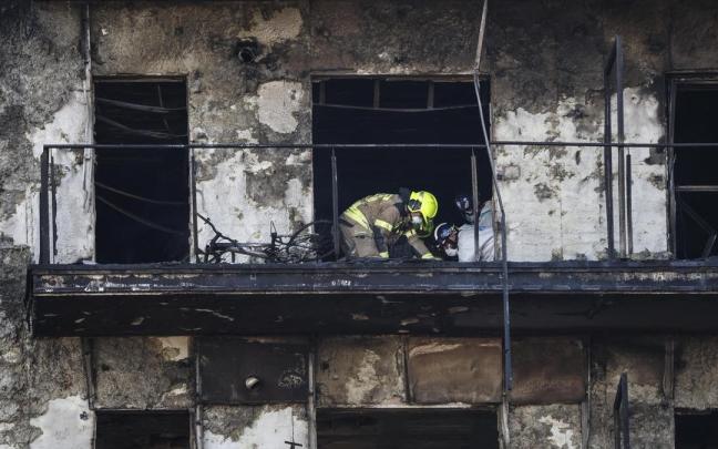 Los bomberos inspeccionan un cuerpo en un balcón del edificio incendiado en Valencia.