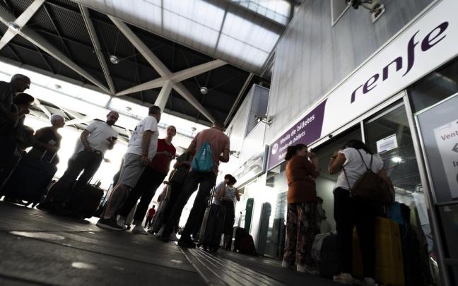Varias personas hacen cola ante una oficina de Renfe en una estación.