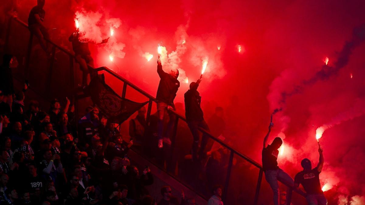 Un grupo de aficionados enciende bengalas en un partido de fútbol.