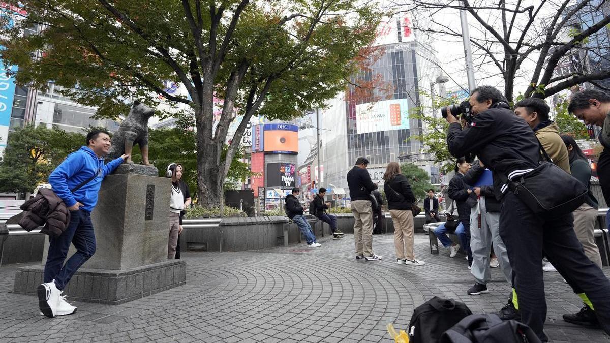 Dos turistas se sacan una foto con la estatua del perro Hachiko en Shibuya.