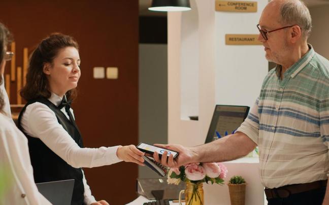 Un hombre paga con su móvil en la recepción de un hotel.