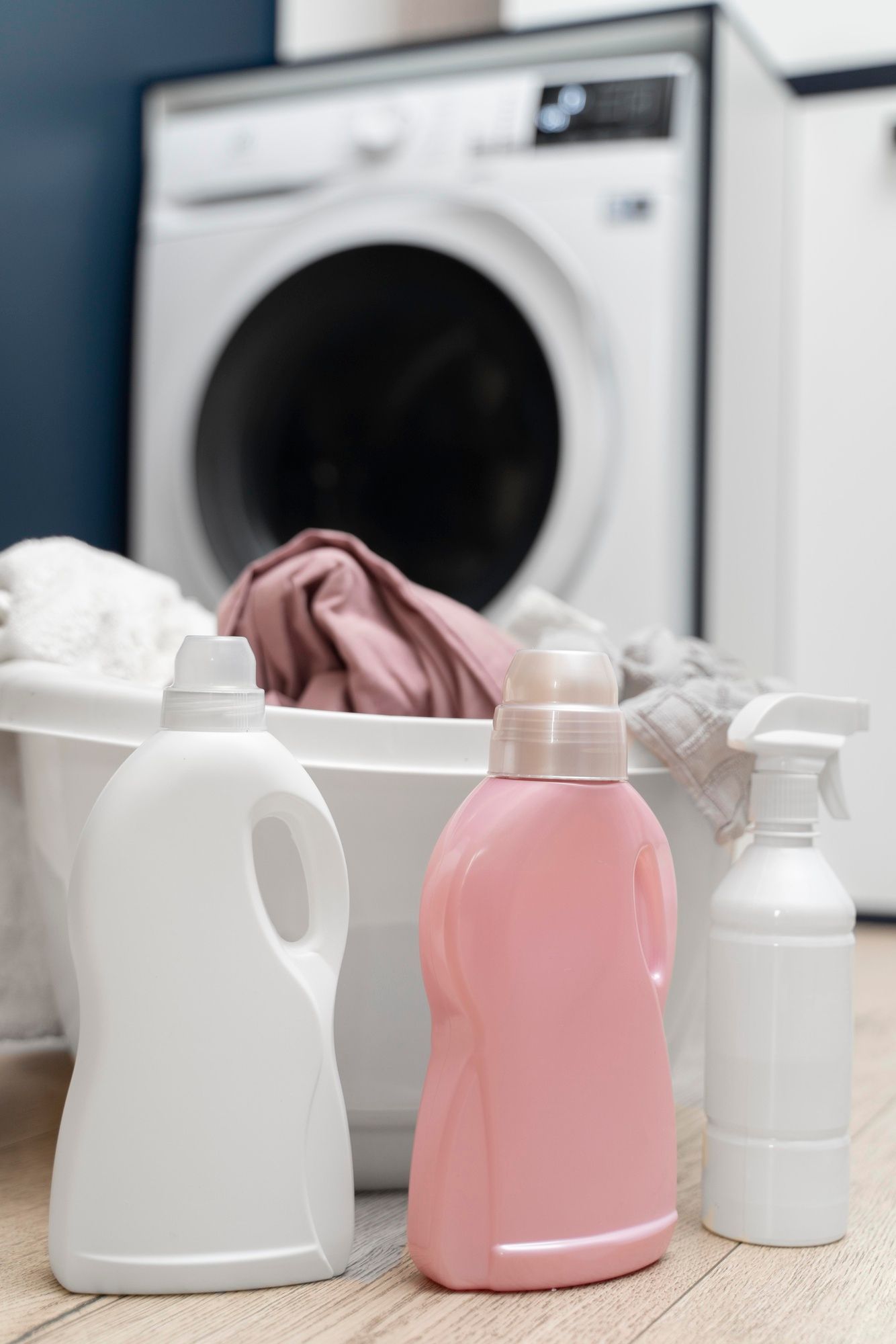 Un balde con ropa sucia,junto a botellas de detergente y quitamanchas delante de una lavadora.