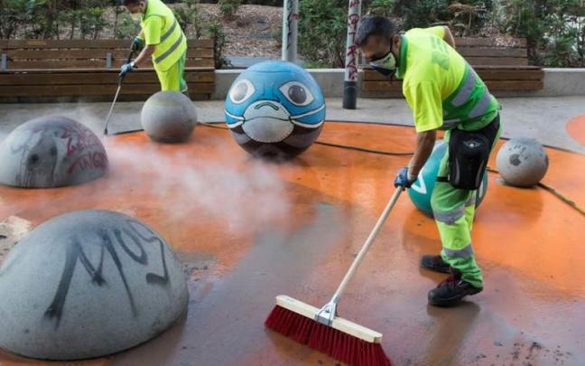 Dos trabajadores limpian una zona de juegos infantiles.