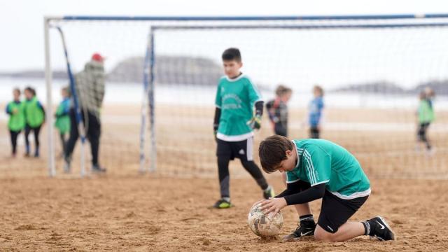 Un menor coloca el balón durante un partido de fútbol en la playa de Zarautz en un campeonato de deporte escolar.