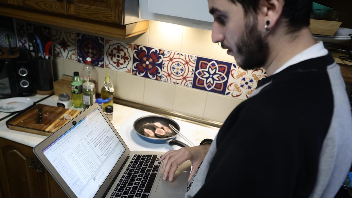 Una persona teletrabaja con su ordenador en la cocina de su domicilio.