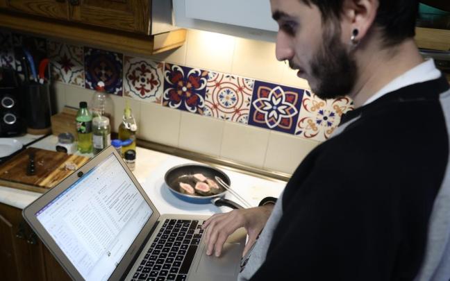 Una persona teletrabaja con su ordenador en la cocina de su domicilio.