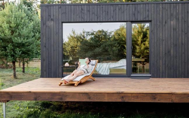 Una mujer descansa en el exterior de una casa prefabricada en el campo.