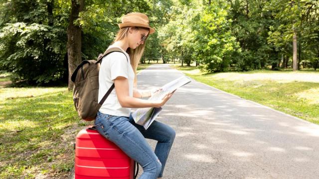Una mujer, sentada sobre su maleta, consulta un mapa en un parque.
