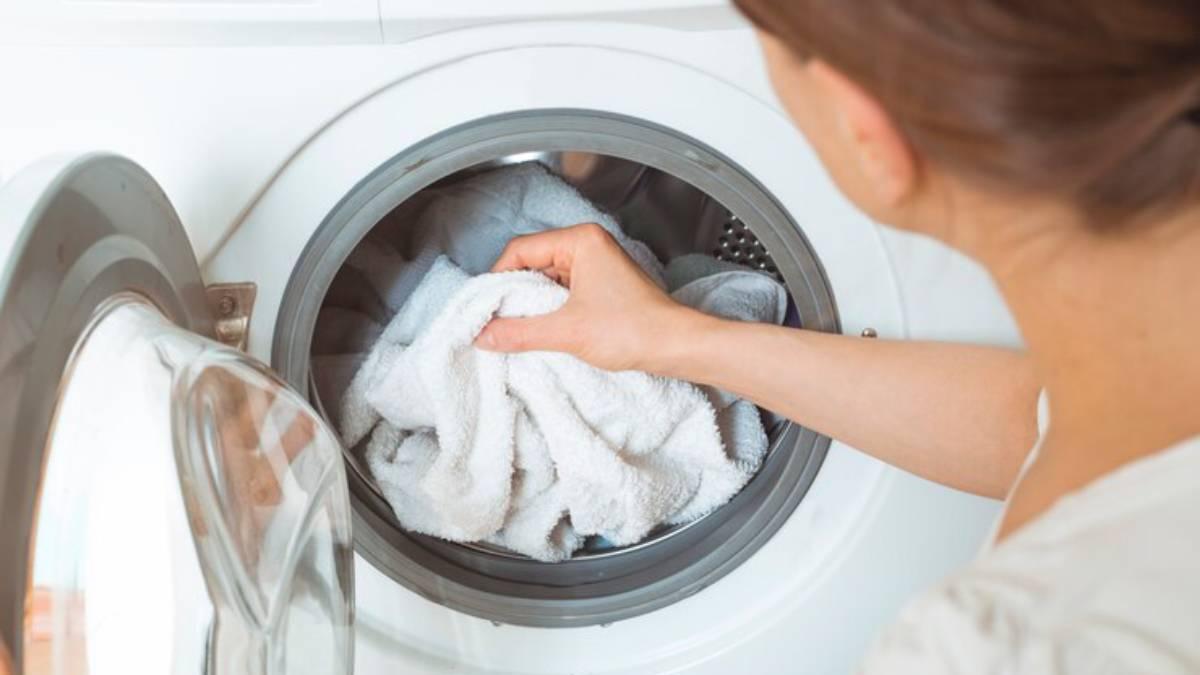 Mujer pone una lavadora con toallas de colores claros