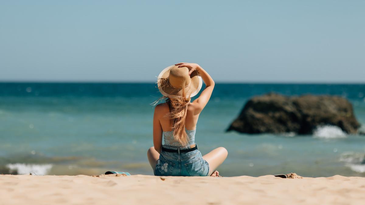 Una mujer se relaja sentada mirando al mar.