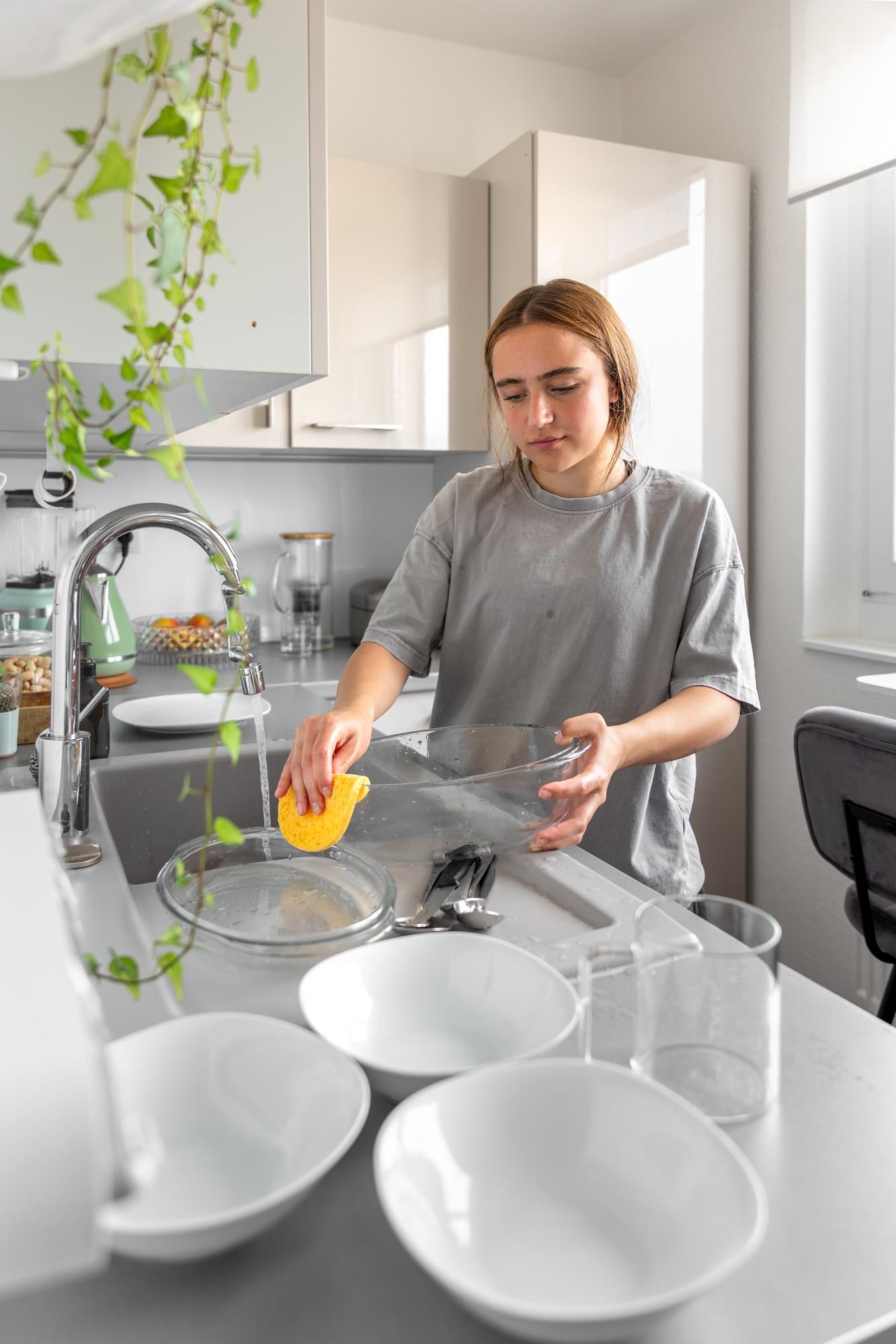 Una chica joven friega un recipiente de cristal en la fregadera.