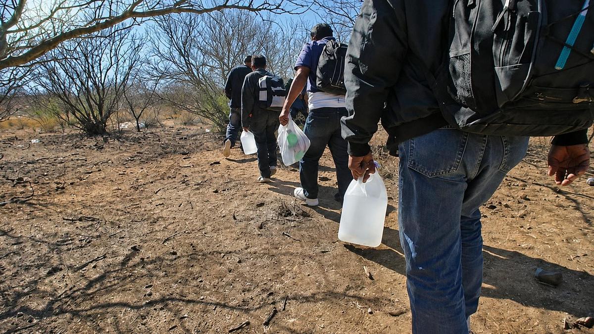 Un grupo de migrantes atraviesa una zona desértica cargado con mochilas y bidones de agua, expuesto a las temperaturas extremas y a los riesgos de las rutas más apartadas.