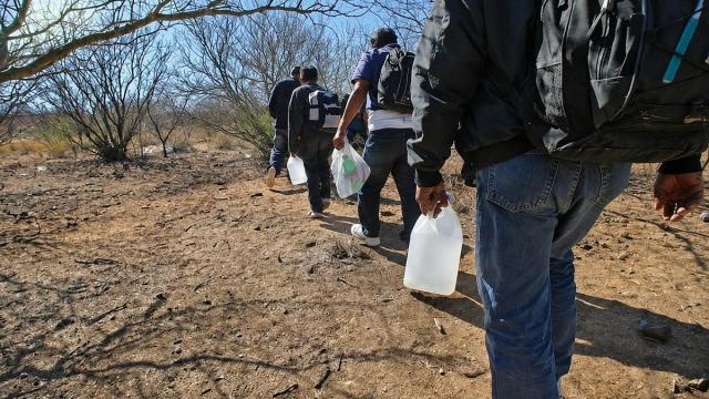 Un grupo de migrantes atraviesa una zona desértica cargado con mochilas y bidones de agua, expuesto a las temperaturas extremas y a los riesgos de las rutas más apartadas.