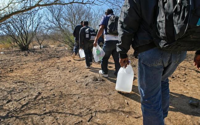 Un grupo de migrantes atraviesa una zona desértica cargado con mochilas y bidones de agua, expuesto a las temperaturas extremas y a los riesgos de las rutas más apartadas.
