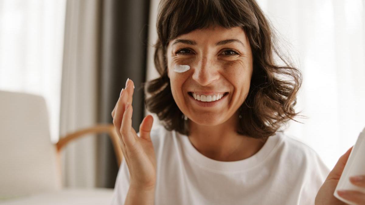 Mujer aplica crema solar en casa antes del maquillaje.