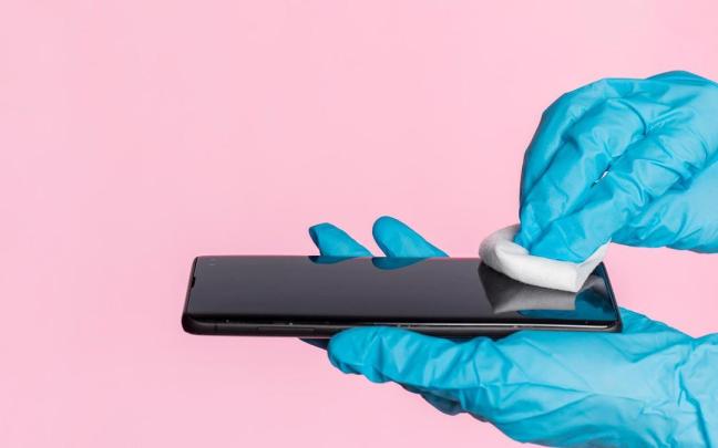 Una persona limpia la pantalla del móvil con guantes y con una toallita.