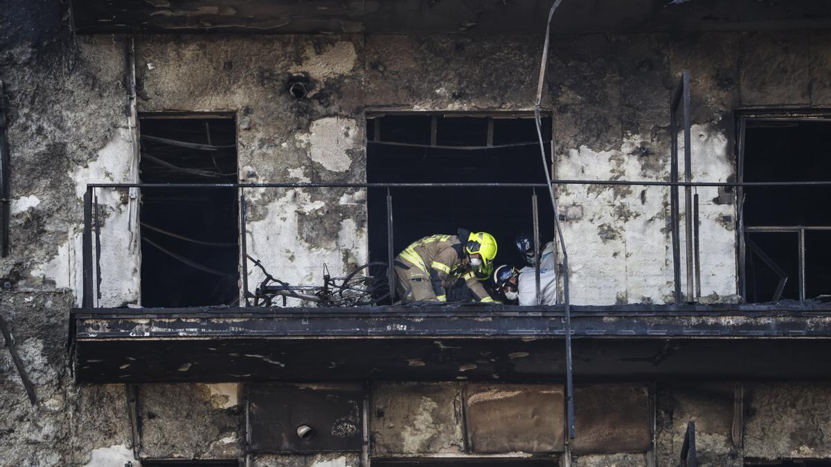 Un bombero y dos agentes de la Policía Científica inspeccionan un cuerpo en un balón del edificio incendiado.