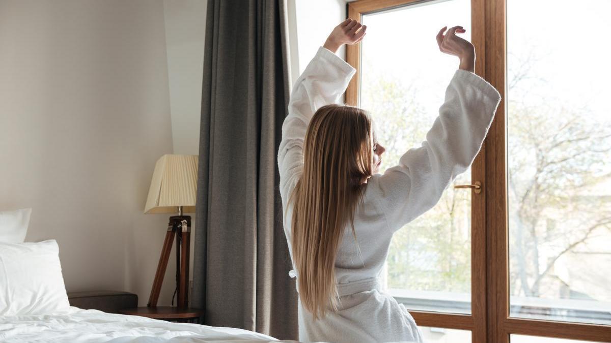 Chica se estira nada más levantarse mientras mira por la ventana de su habitación