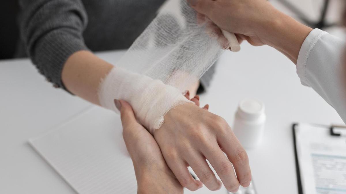 Una sanitaria venda la muñeca a una paciente.