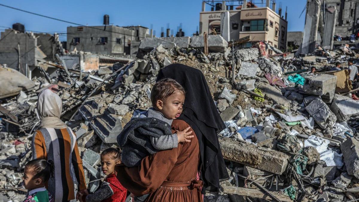 Dos mujeres palestinas inspeccionan junto a sus hijos los restos de una vivienda destruida en Rafah.