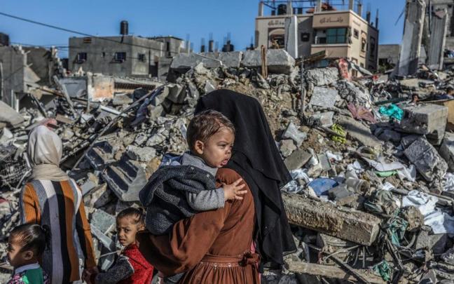 Dos mujeres palestinas inspeccionan junto a sus hijos los restos de una vivienda destruida en Rafah.