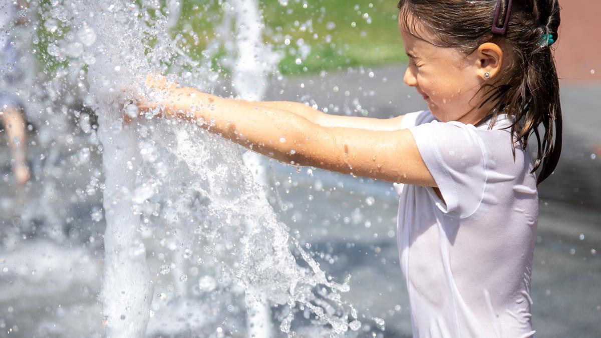 Una niña se refresca en una fuente.