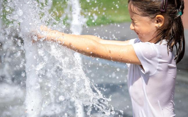 Una niña se refresca en una fuente. Una niña se refresca en una fuente.