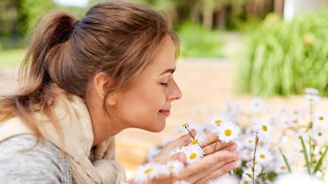 Primer plano de una mujer tratando de oler unas flores.
