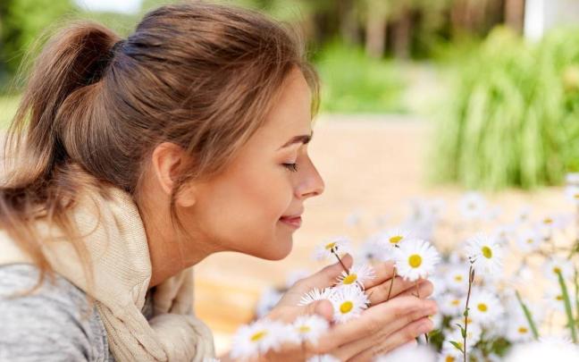 Primer plano de una mujer tratando de oler unas flores.