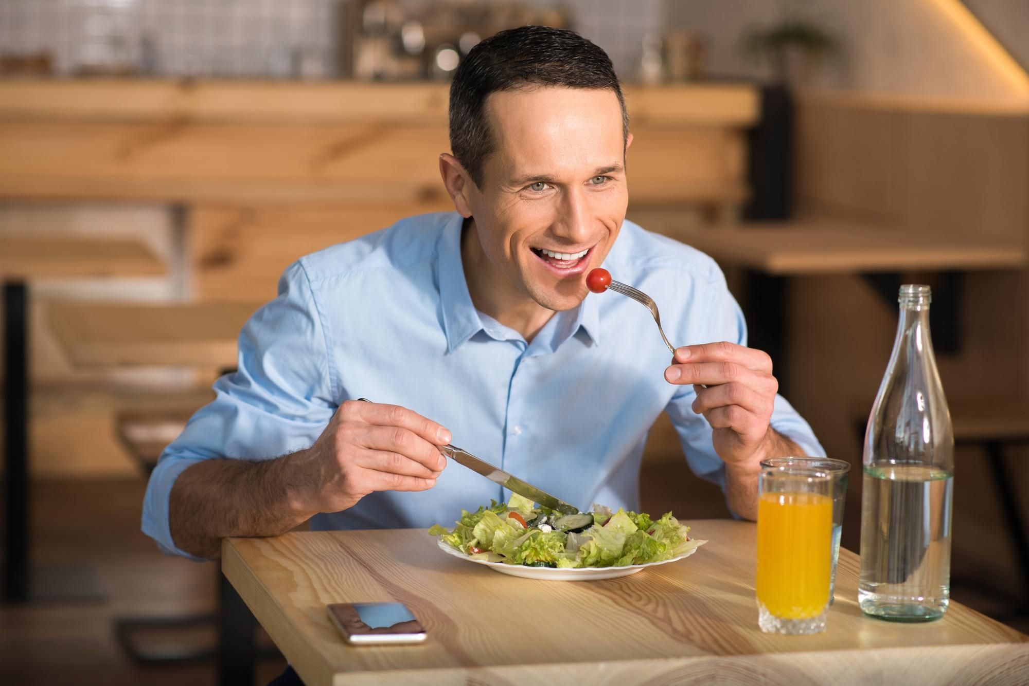 Un hombre degusta una ensalada con un zumo y agua.