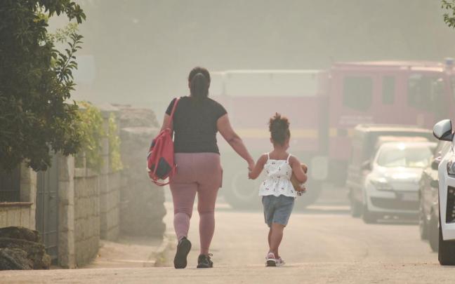 Una madre y una niña camina de la mano en Burgohondo (Ávila) entre el humo del incendio que continúa fuera de la capacidad de extinción.
