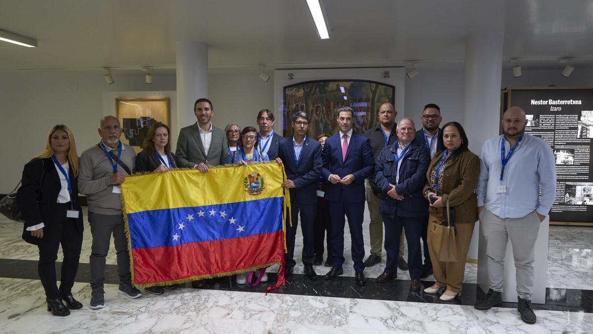 El parlamentario del PNV Mikel Arruabarrena, sosteniendo la bandera de Venezuela, y el lehendakari Pradales, con colectivos de venezolanos en el Parlamento Vasco