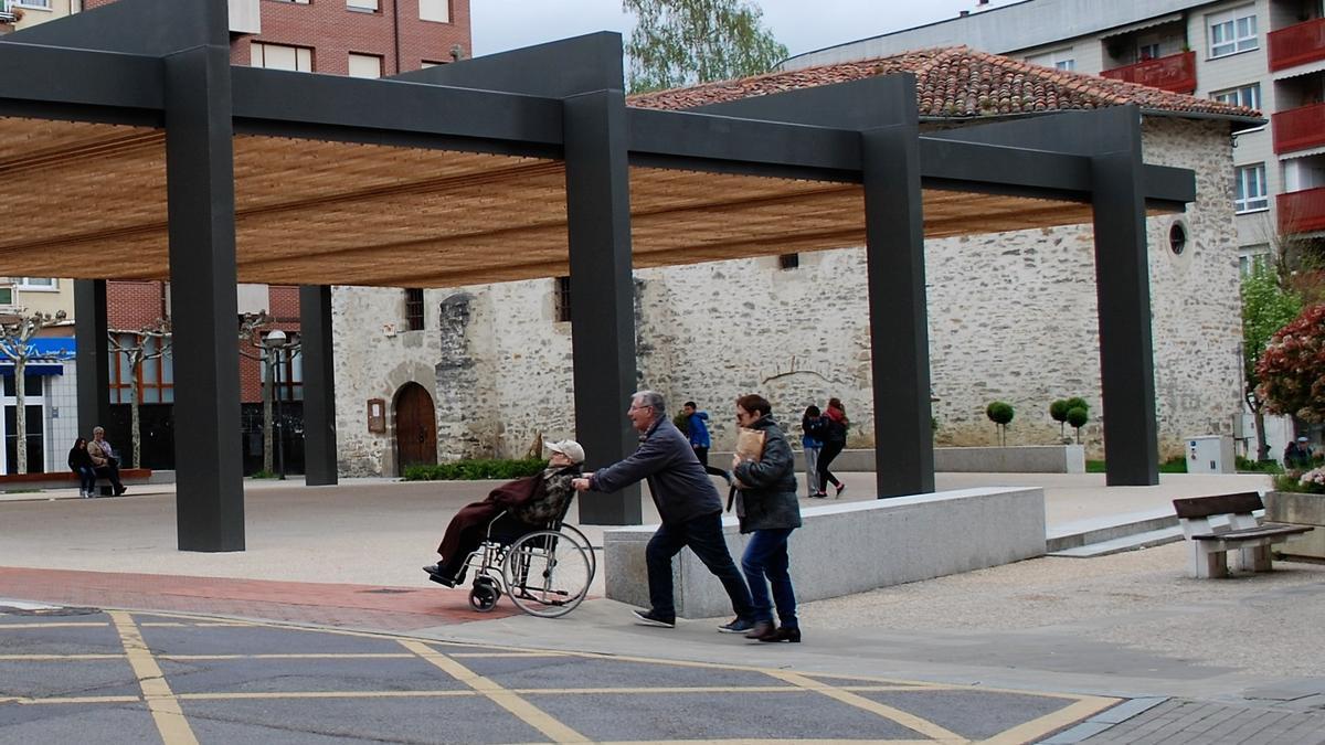 Una pareja traslada a un anciano en silla de ruedas por la plaza San Antón de Amurrio