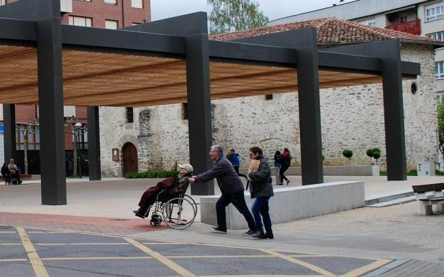 Una pareja traslada a un anciano en silla de ruedas por la plaza San Antón de Amurrio