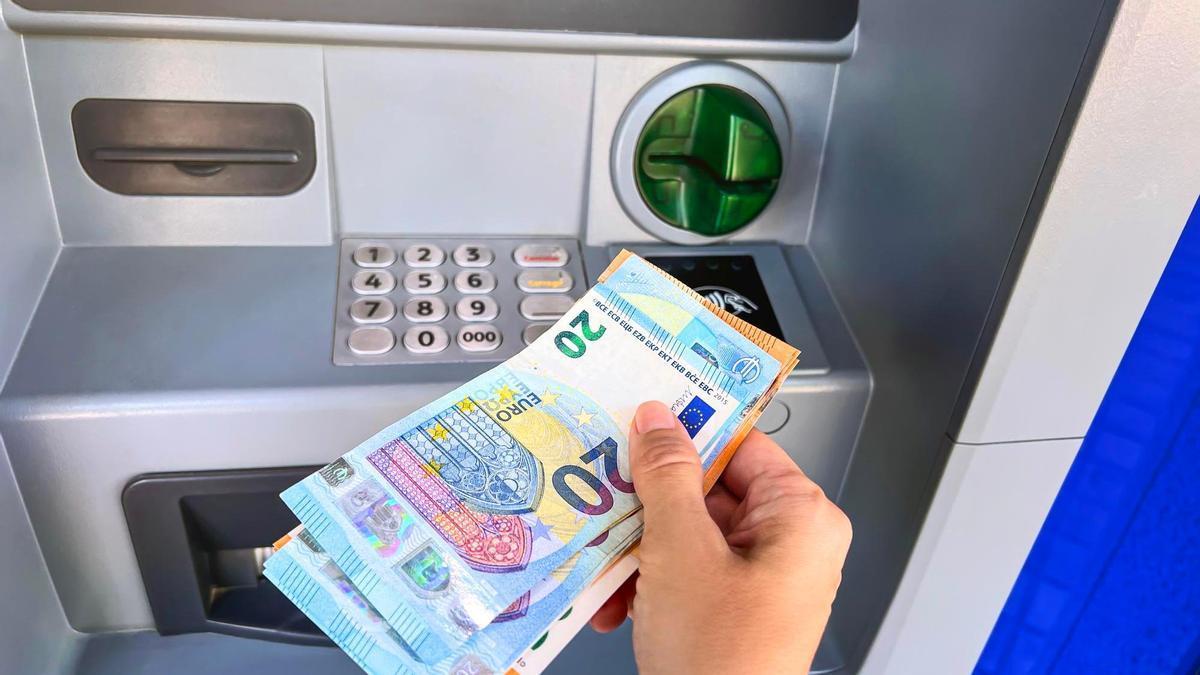 Una persona tiene en su mano varios billetes junto a un cajero automático.