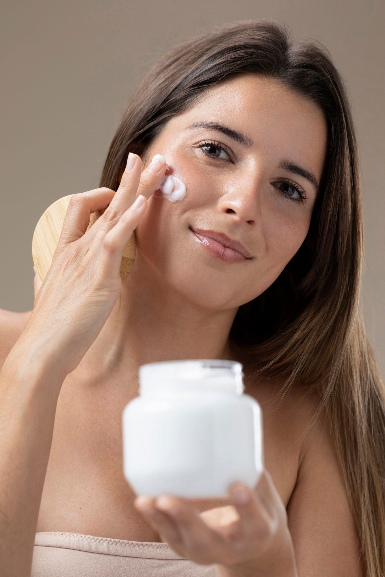 Una mujer se aplica crema hidratante en el rostro.