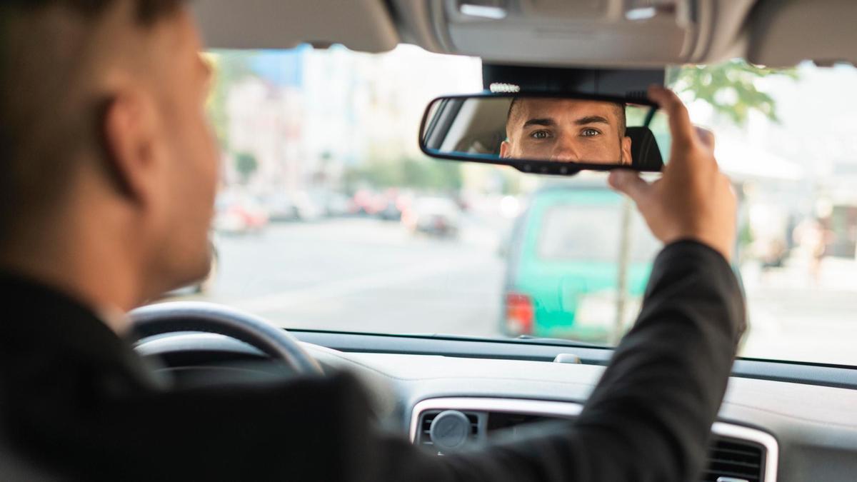 Un hombre se coloca el espejo retrovisor en la posición correcta.