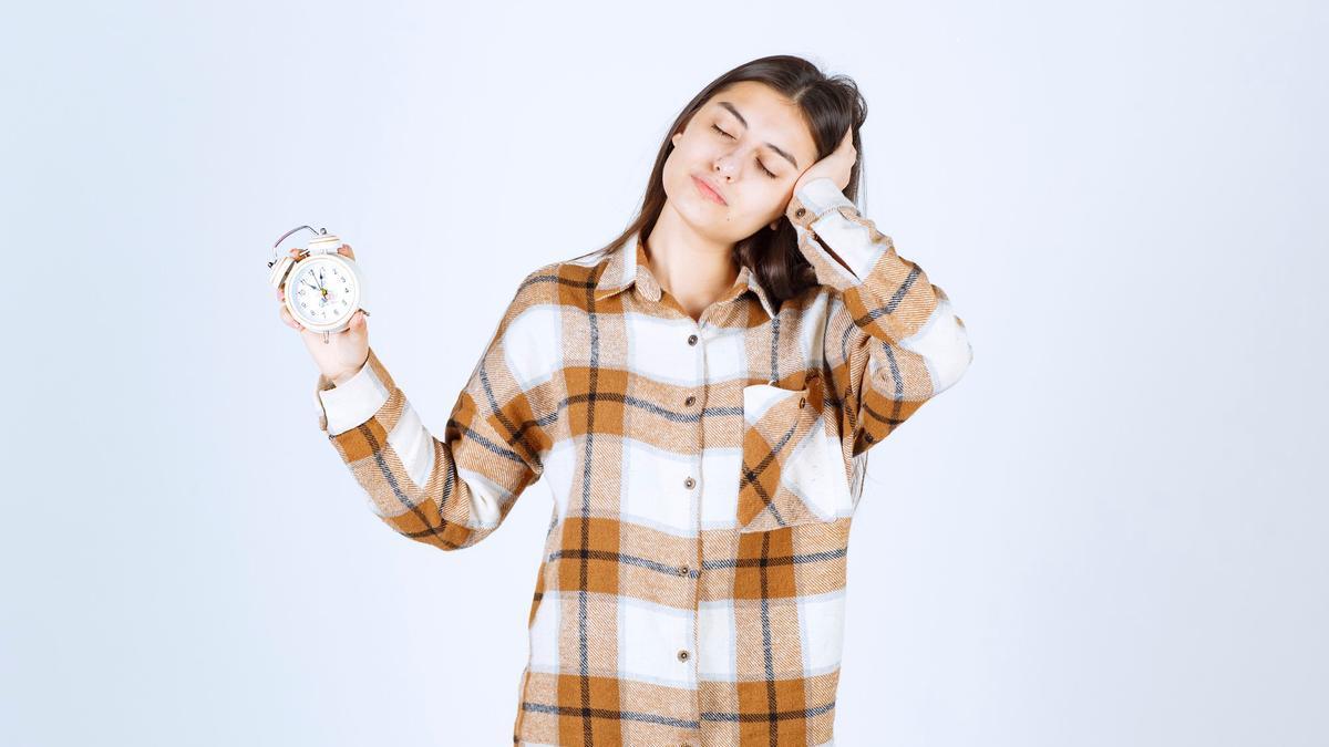 Una mujer, somnolienta, sujeta un pequeño reloj con la mano.